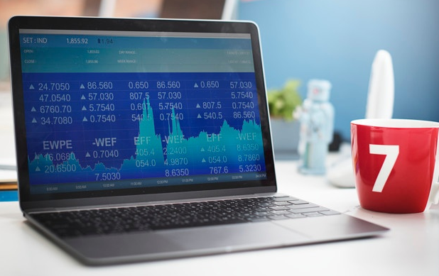 notebook com gráficos de valorização de ações ao lado de uma caneca vermelha em cima de uma mesa