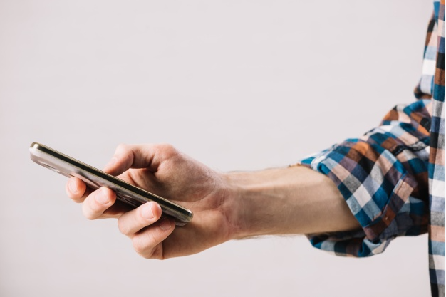 imagem ampliada de mão e braço de uma pessoa vestindo uma camiseta xadrez segurando um celular