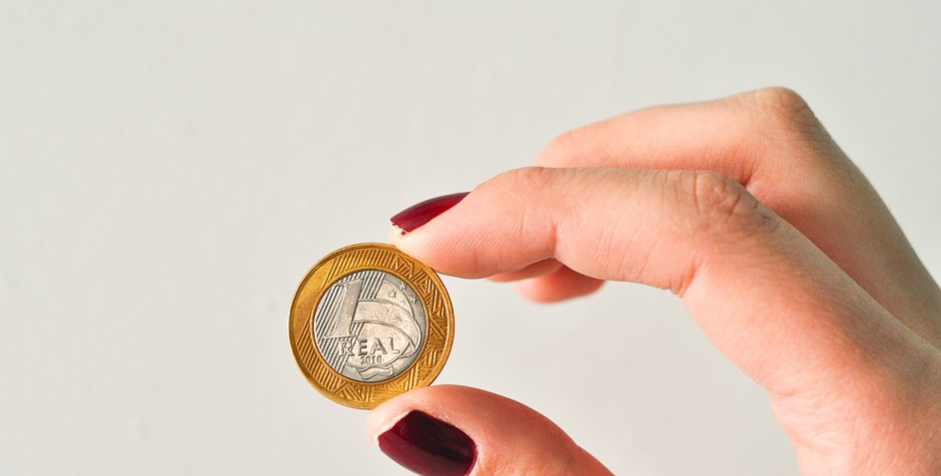 mãos femininas segurando uma moeda de 1 real apenas com o polegar e o dedo anelar