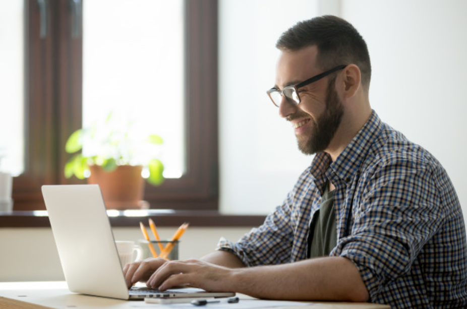 homem de camisa listrada e óculos sorrindo enquanto usa seu laptop