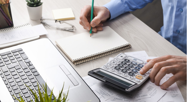 imagem ampliada da mesa de um empresário com uma calculadora e um bloco de notas em frente a um computador