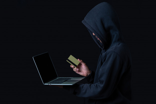 Pessoa encapuzada com um cartão de crédito e um laptop
