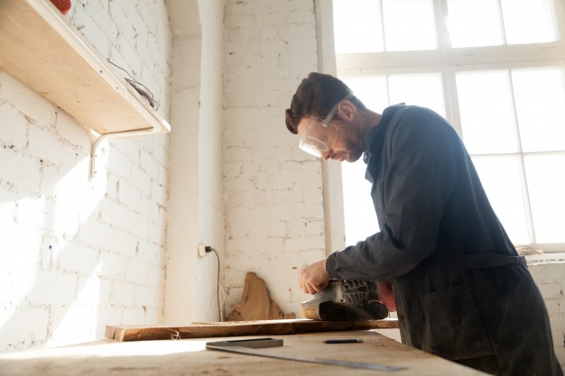 marceneiro equipado com proteção serra um pedaço de madeira em sua oficina