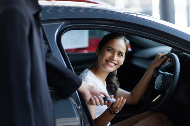 mulher de branco sorrindo dentro de carro enquanto recebe a chave do veículo de um homem de terno