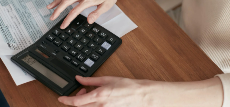 imagem ampliada de mulher sentada à mesa mexendo na calculadora com um papel em baixo da calculadora