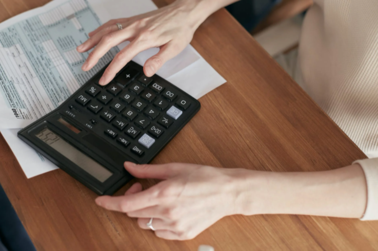 imagem ampliada de mulher sentada à mesa mexendo na calculadora com um papel em baixo da calculadora