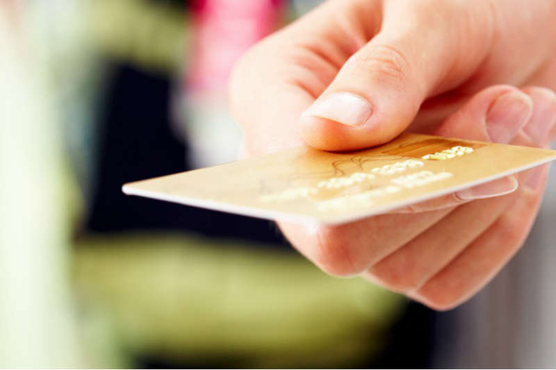 imagem com destaque para uma mão que segura um cartão de crédito.