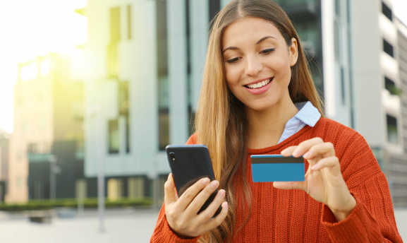 mulher loira usando suéter vermelhos usando o cartão mercado livre para fazer compras online com seu celular