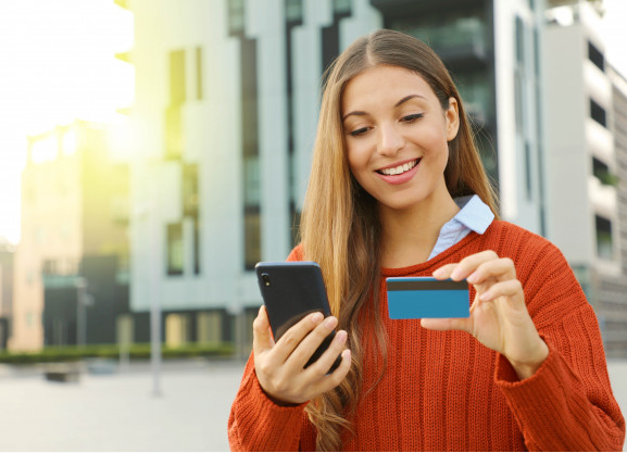 mulher loira usando suéter vermelhos usando o cartão mercado livre para fazer compras online com seu celular