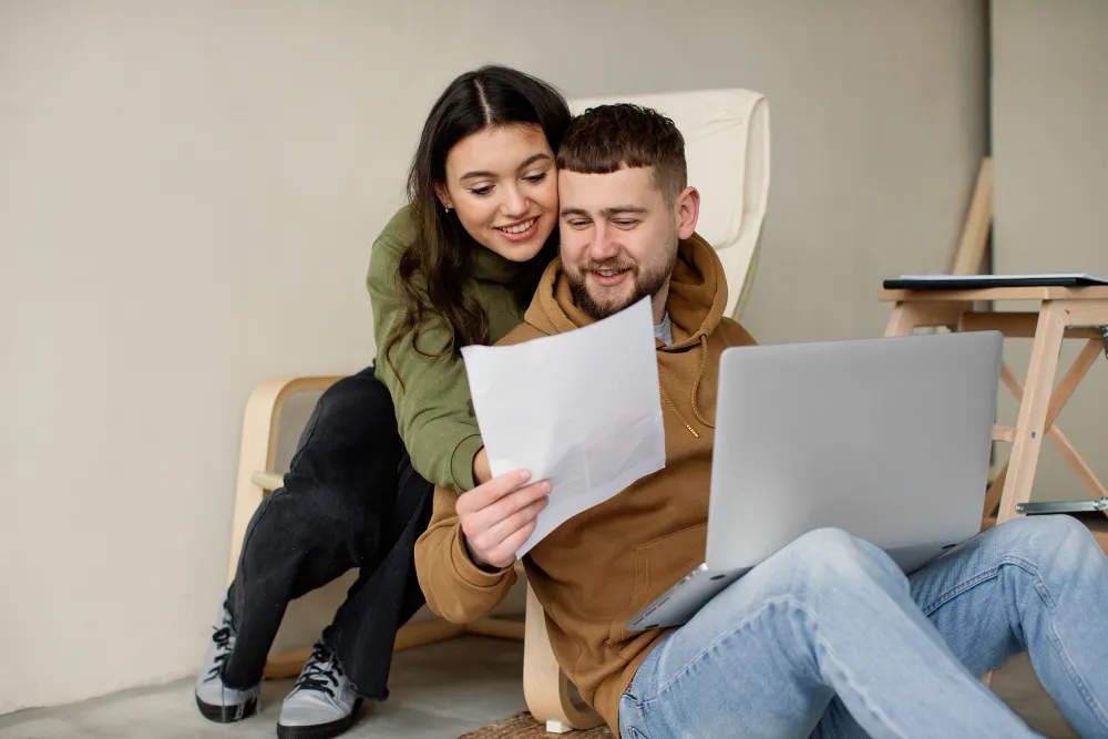 casal abraçados enquanto ele, com um notebook no colo, mostra um papel para ela o que é empréstimo consignado