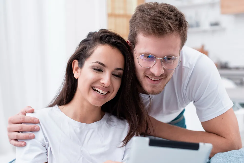 casal feliz e sorridente, o homem abraça ela de lado enquanto ela mexe num tablet - simular empréstimo consignado