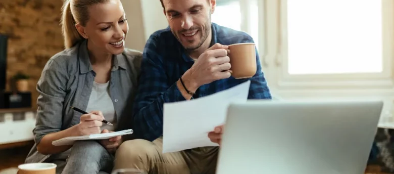 casal sentado na sala de casa, com café e papeis nas mãos, em frente ao computador - simular empréstimo consignado