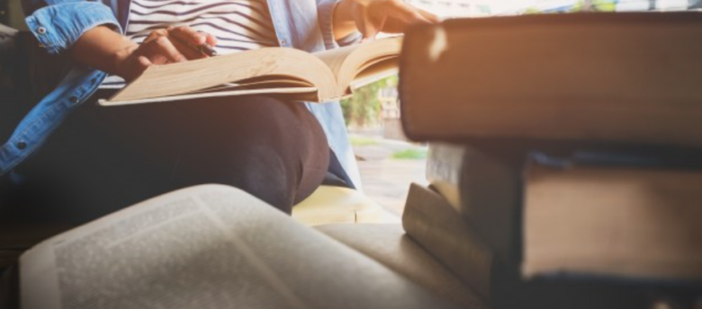 imagem ampliada de uma mulher sentada lendo livros ao lado de uma mesa cheia de outros exemplares