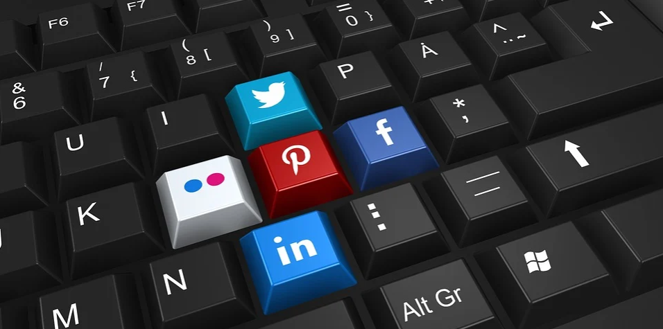 imagem de teclado preto com cinco teclas contendo os simbolos do twitter, facebook, pinterest, linkedin e uma tecla branca com bolas vermelhas e azuis desenhadas