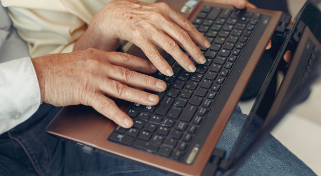 imagem ampliada de idosos colocando suas mãos sobre um computador que está em seu colo