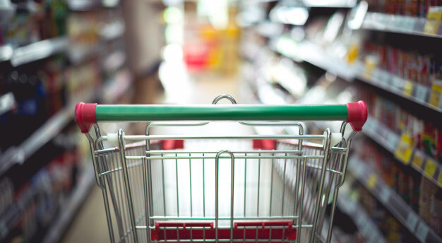 imagem de carrinho de supermercado vazio em primeiro plano e ao fundo um corredor de supermercado desfocado
