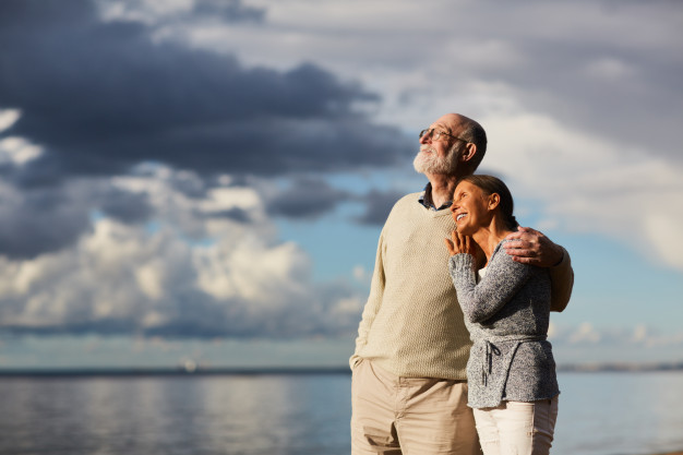 casal de idosos se abraça de frente pro mar e olhando o céu