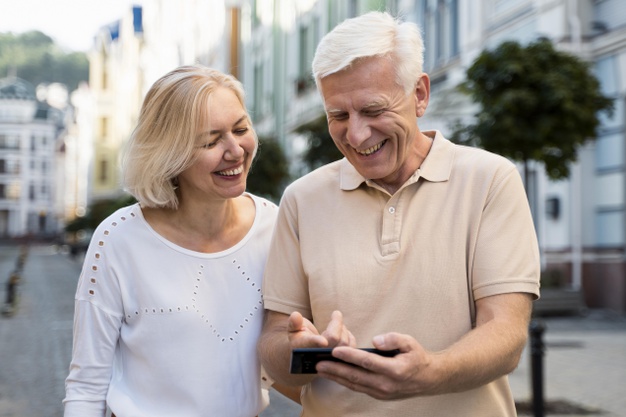 casal de aposentados sorri enquanto olha para um celular