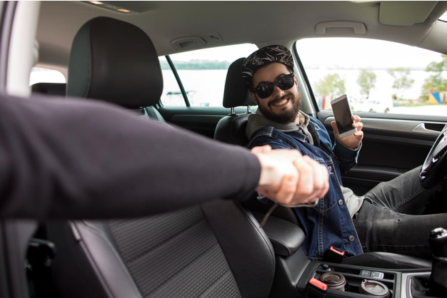 homem de boné que trabalha como motorista de aplicativo sorri enquanto cumprimenta homem de terno que sai de seu carro