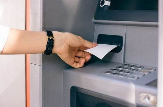 mão retirando extrato bancário em papel liberado pelo caixa eletrônico.