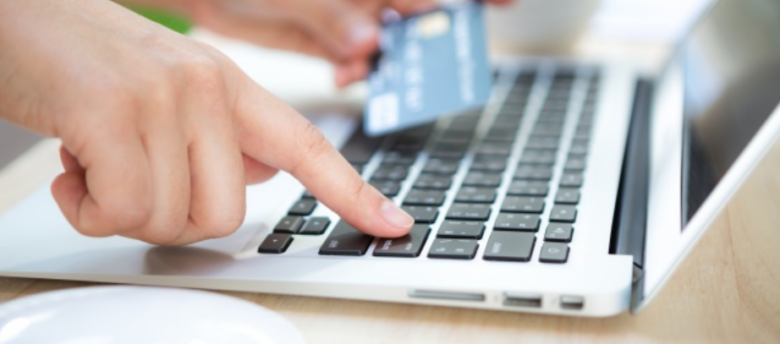 imagem ampliada de uma mulher segurando um cartão de crédito e digitando em um laptop