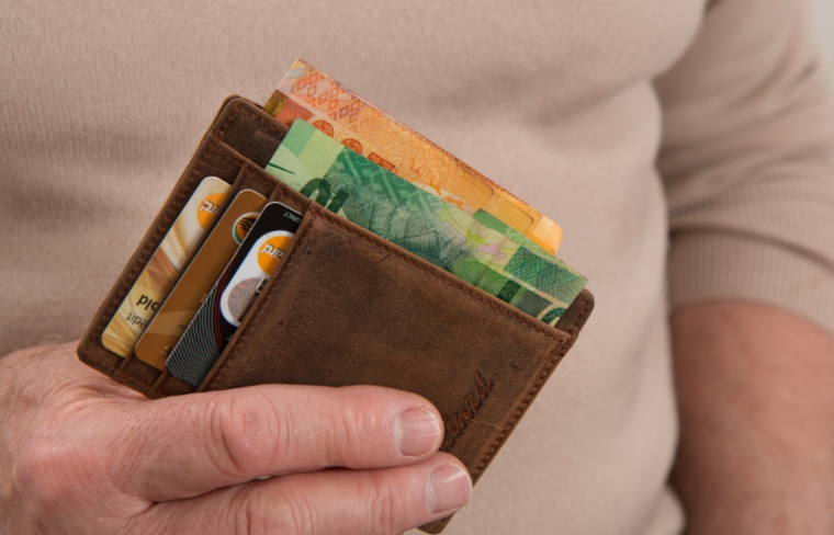 Pessoa com uma carteira com dinheiro e cartão de crédito em uma das mãos.