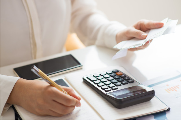 mulher sentada a uma mesa com celular e calculadora fazendo conta para pagamento de dívidas