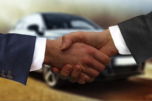 imagem de um carro ao fundo e duas mãos à frente firmando um acordo