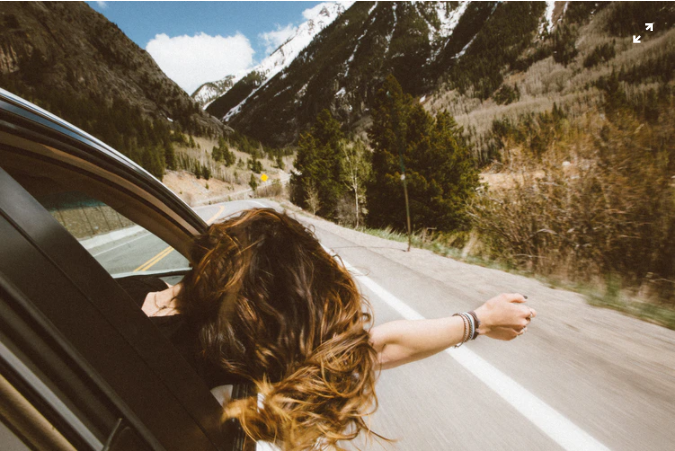 mulher colocando a cabeça para fora através da janela de carro em uma estrada