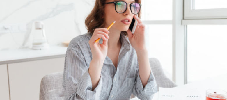 mulher de óculos de camisa cinza falando ao telefone segurando um lápis em sua mão direita