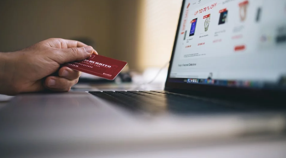 tela de computador com um ecommerce na tela e uma mão segurando um cartão de crédito para realizar compra online