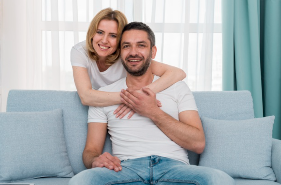 imagem de um homem sentado em um sofá sendo abraçado por uma mulher