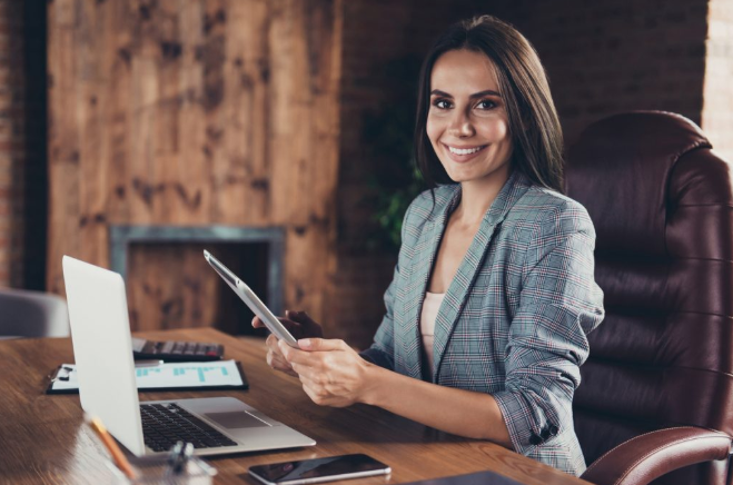 mulher de terno sorrindo trabalhando em frente ao seu laptop