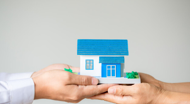 dois pares de mãos dividindo uma casa em miniatura azul e branca