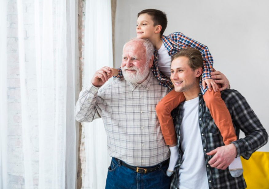 trio de diferentes gerações de uma familia composto por avô, pai e filho parados em frente a uma janela