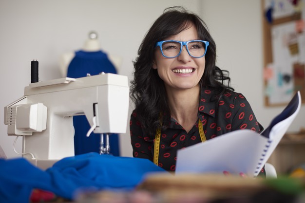 imagem de mulher de óculos sentada a uma mesa com uma máquina de costura