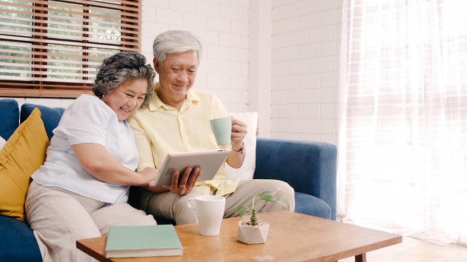casal de idosos usando tablet sentados em sofá azul