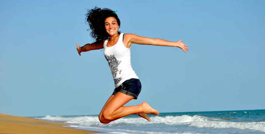 imagem de mulher saltando na praia bem tranquila e feliz. Aparentemente porque pediu empréstimo na caixa
