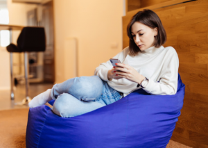 imagem de uma mulher fazendo empréstimo online através do celular deitada em uma almofada violeta