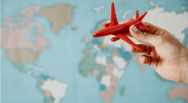 pessoa segura avião vermelho em miniatura e o move por cima de um mapa mundi