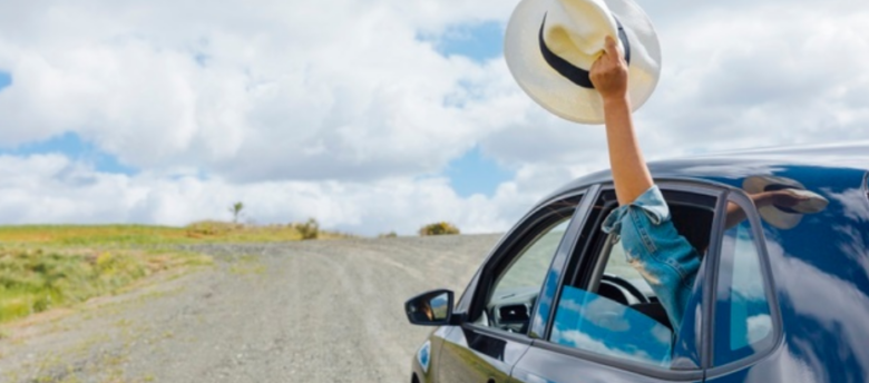 pessoa estendendo o braço segurando chapéu de dentro de um carro em movimento em uma rodovia