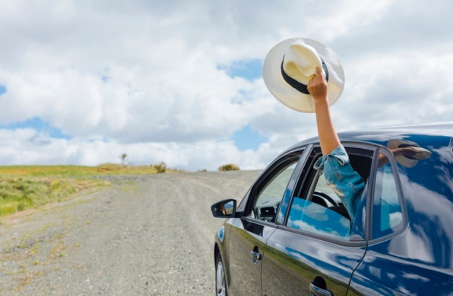 pessoa estendendo o braço segurando chapéu de dentro de um carro em movimento em uma rodovia