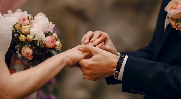 imagem ampliada de um noivo colocando uma aliança em sua noiva durante um casamento