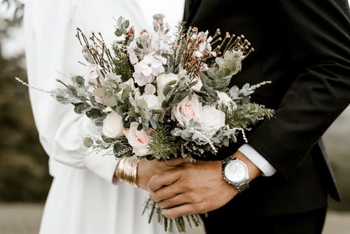 imagem ampliada de um noivo e uma noiva segurando um bouquet de flores juntos