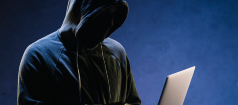 imagem de homem de roupas pretas coberto com capuz usando um laptop
