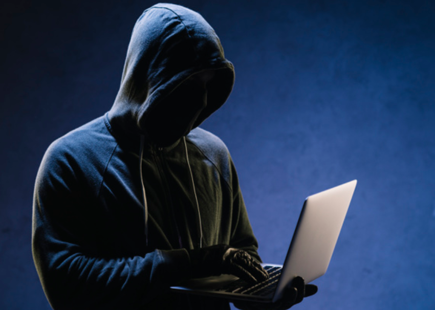 imagem de homem de roupas pretas coberto com capuz usando um laptop