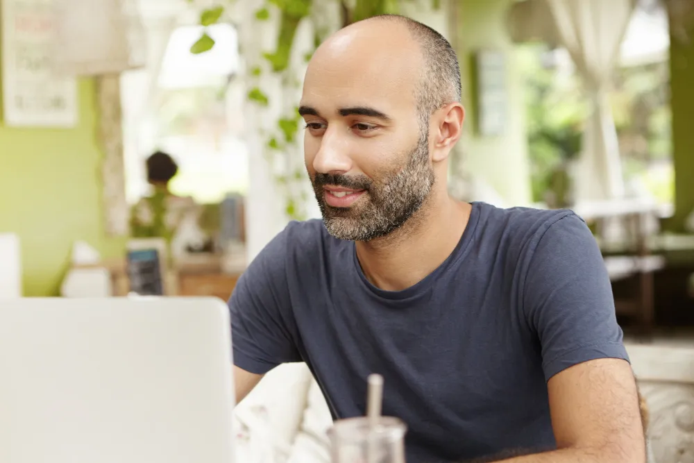 homem careca usando computador em café ao ar livre - qual banco libera cartão de crédito para negativado