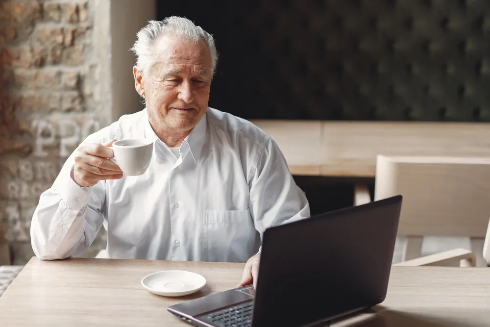 homem de idade trabalhando no computador enquanto toma um café - lei do empréstimo consignado em folha de pagamento