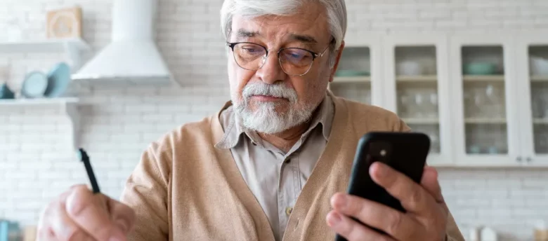 homem de terceira idade com o celular na mão e escrevendo com a outra - quanto um aposentado pode pegar de empréstimo