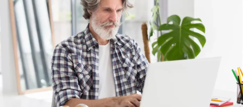 homem grisalho com barba sentado mexendo em notebook como reduzir parcelas de empréstimo consignado